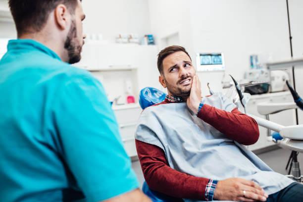 a man holding his jaw due to toothache while looking at the dentist
