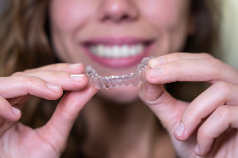 A blurred woman holding an Invisalign aligner in front of her face