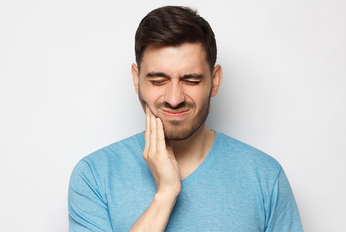 Man in blue shirt rubbing jaw in pain.