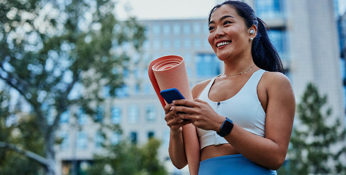 Smiling woman with yoga mat walking in park.